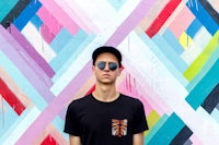 a young man in a black t - shirt standing in front of a colorful wall